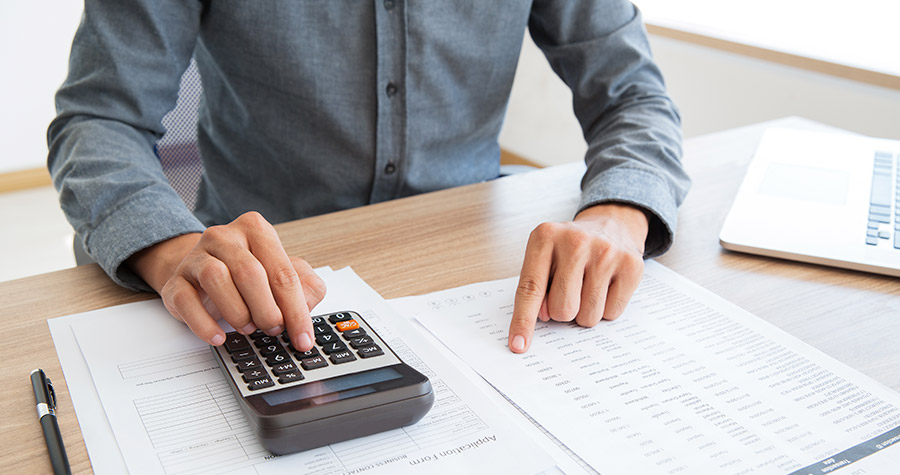 homem sentado em frente a uma mesa com papeis e uma calculadora calculando os custos de transporte