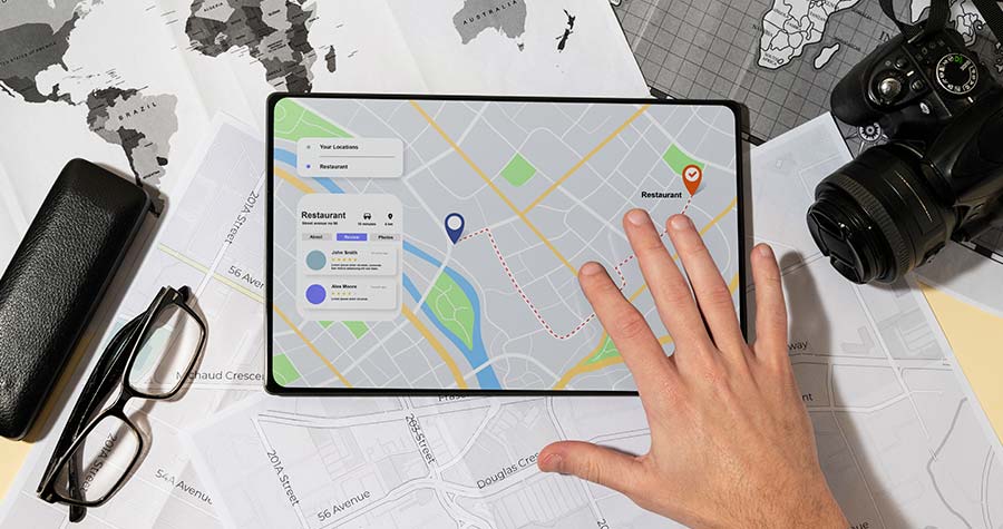 ao fundo um mapa e sobre ele um tablet com imagem de gps e uma mão masculina mexendo realizando a roteirização de cargas